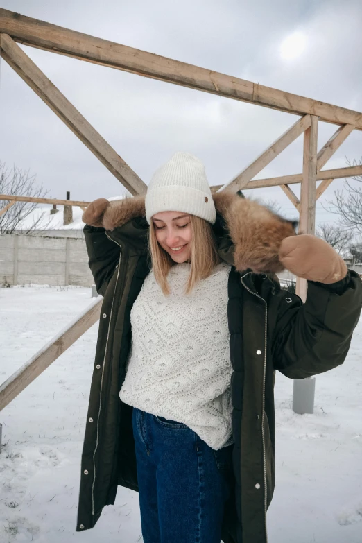 a woman that is standing in the snow, wearing a white sweater, beige hoodie, wearing farm clothes, arhitectural shot