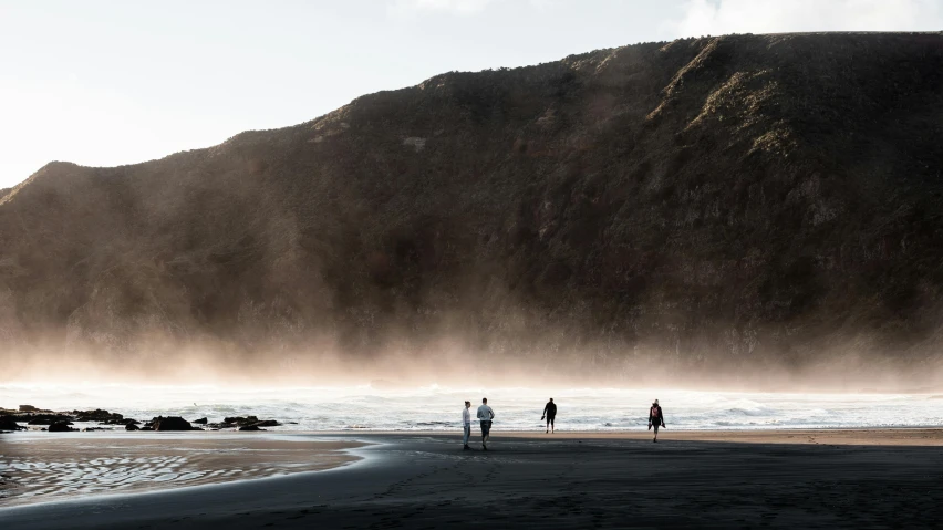 a group of people standing on top of a sandy beach, by Peter Churcher, unsplash contest winner, te pae, coastal cliffs, people running away, late morning