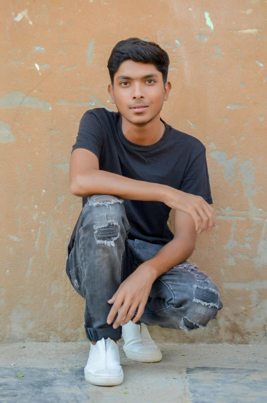 a young man sitting on the ground in front of a wall, by Rajesh Soni, jeans and t shirt, south east asian with round face, 15081959 21121991 01012000 4k, black teenage boy