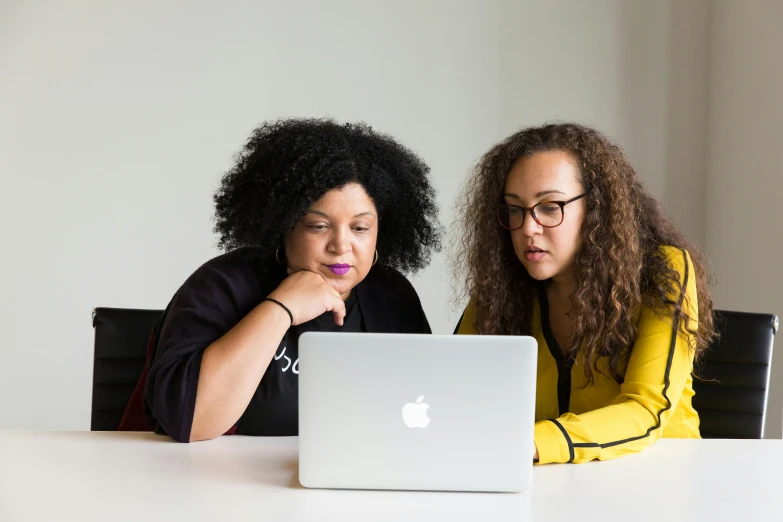 two women sitting at a table looking at a laptop, by Carey Morris, pexels, square, black, apple, essence