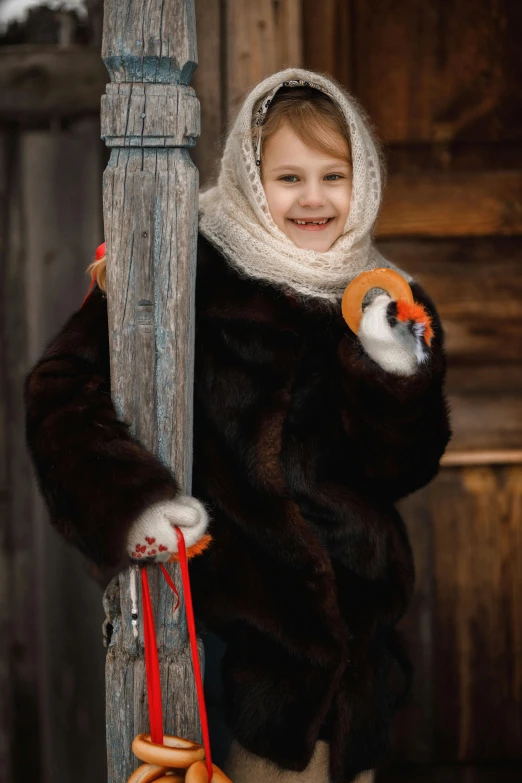 a little girl that is standing next to a pole, a portrait, inspired by Carl Larsson, pexels contest winner, fur scarf, pinguin, brown, portrait image