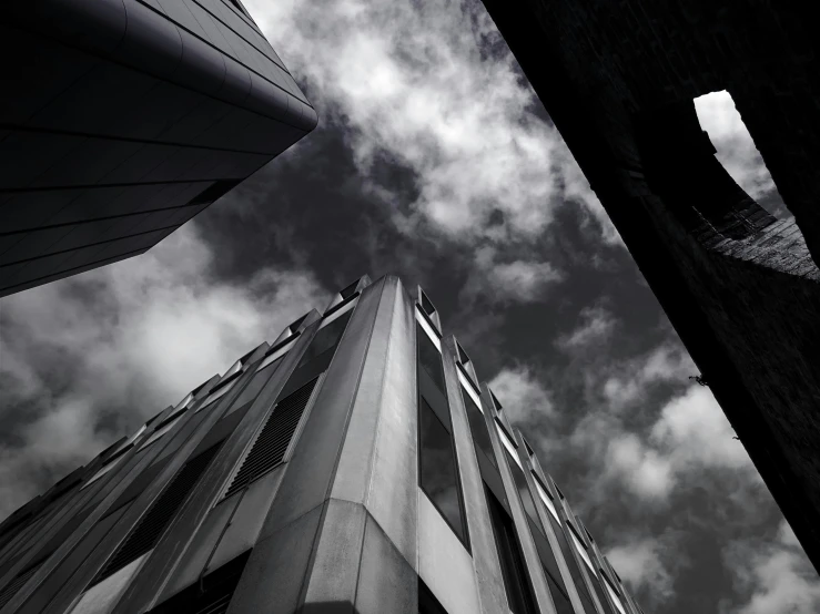 a black and white photo of a tall building, by Dave Allsop, unsplash, grey clouds, te pae, falling buildings, corners