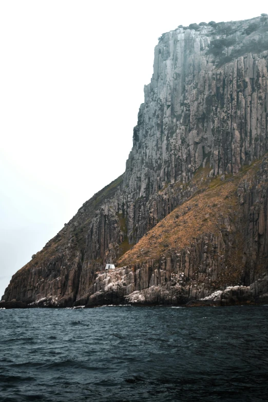 a large rock in the middle of a body of water, by Elsa Bleda, unsplash, in socotra island, steep cliffs, 4k”, grey
