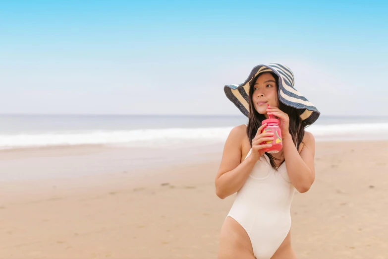 a woman standing on top of a sandy beach, drinking a strawberry iced latte, wearing a silly hat, charli xcx, skincare