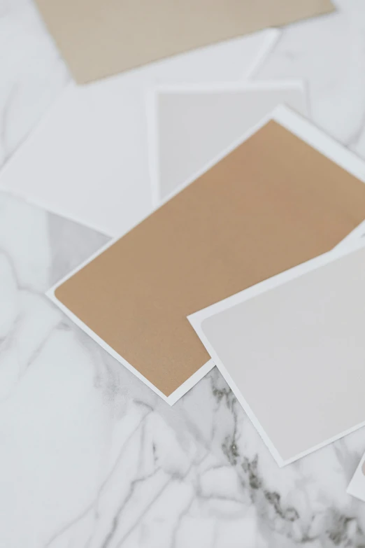 a pile of cards sitting on top of a marble table, brown and white color scheme, paper border, no - text no - logo, curated collections