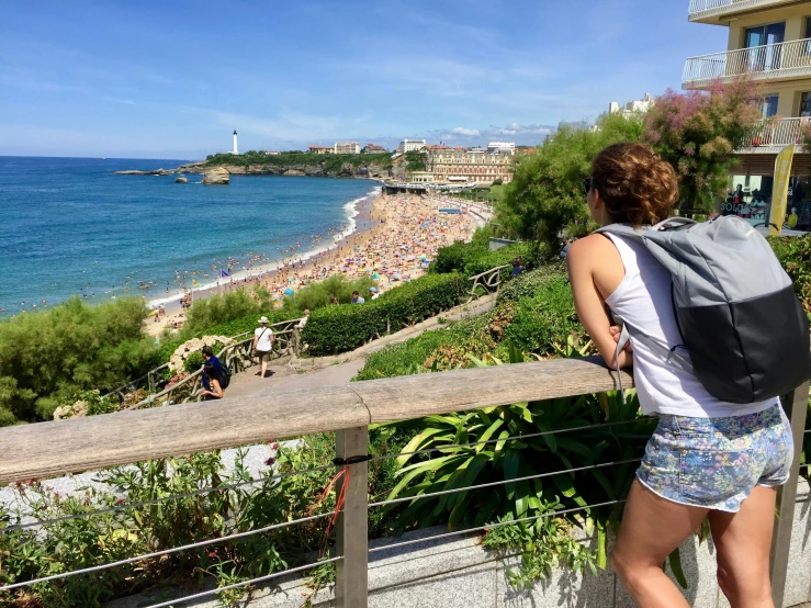 a woman with a backpack looking at the beach, a picture, entire city in view, la nouvelle vague, profile image