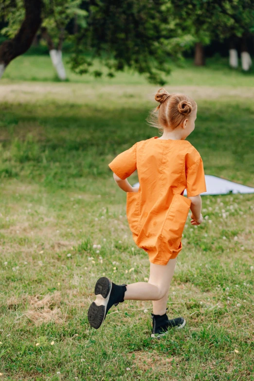 a little girl running in a field with a kite, inspired by Christo, pexels contest winner, happening, wearing orange prison jumpsuit, wearing track and field suit, back view also, short sleeves