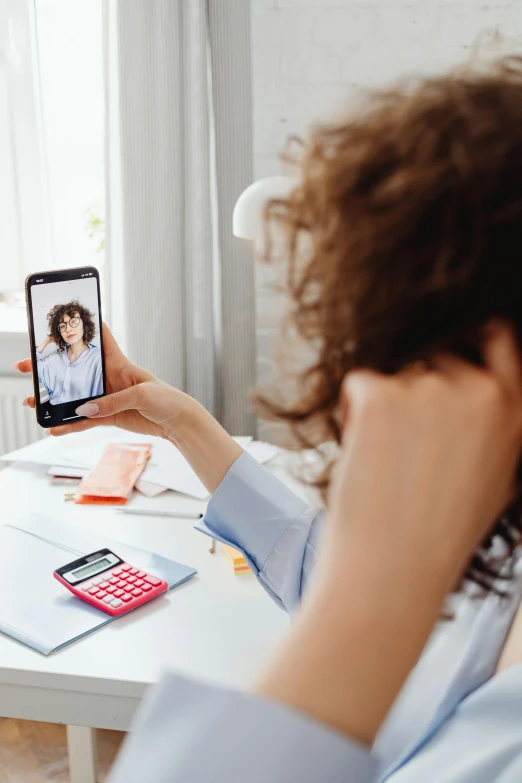 a woman taking a picture of herself on her phone, trending on pexels, surrealism, brown curly hair, sitting behind desk, healthcare, trending on tiktok