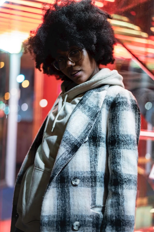 a woman standing in front of a store window, inspired by Gordon Parks, trending on pexels, tartan hoodie, shot at night with studio lights, african american young woman, promotional image