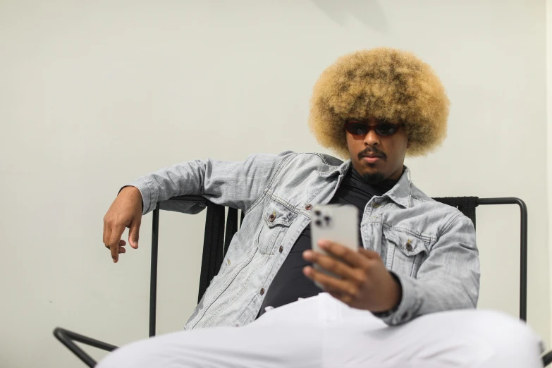 a man sitting in a chair with a cell phone, trending on unsplash, afrofuturism, short blonde afro, drdisrespect posing as napoleon, catalog photo, giant afro!