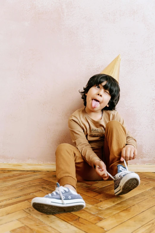 a little boy sitting on the floor with a cone on his head, pexels contest winner, licking tongue, brown pants, wearing a party hat, islamic