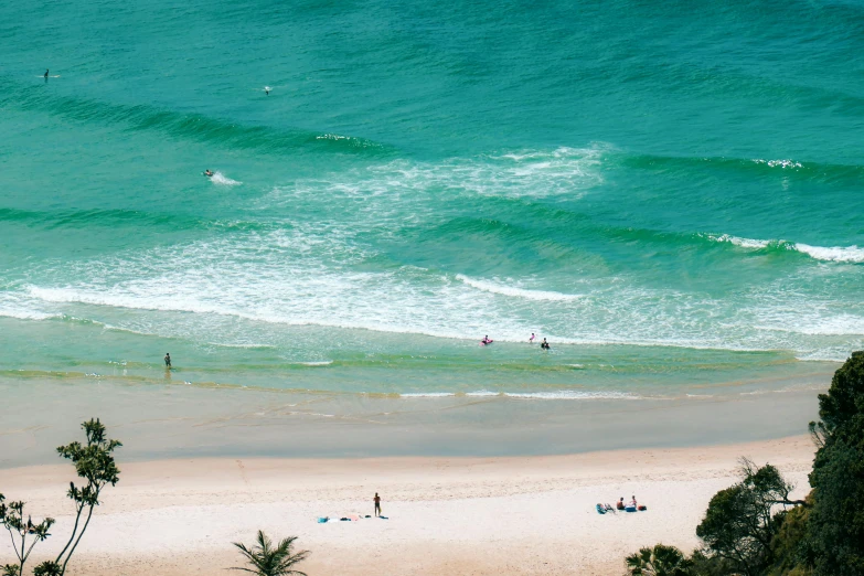 a group of people standing on top of a beach next to the ocean, lush green, gold coast australia, swimming in ocean, minimalist