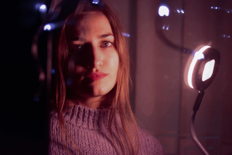 a woman holding a light in front of her face, inspired by Elsa Bleda, pexels contest winner, photorealism, infinity mirror, side portrait of imogen poots, purple scene lighting, ana de armas portrait