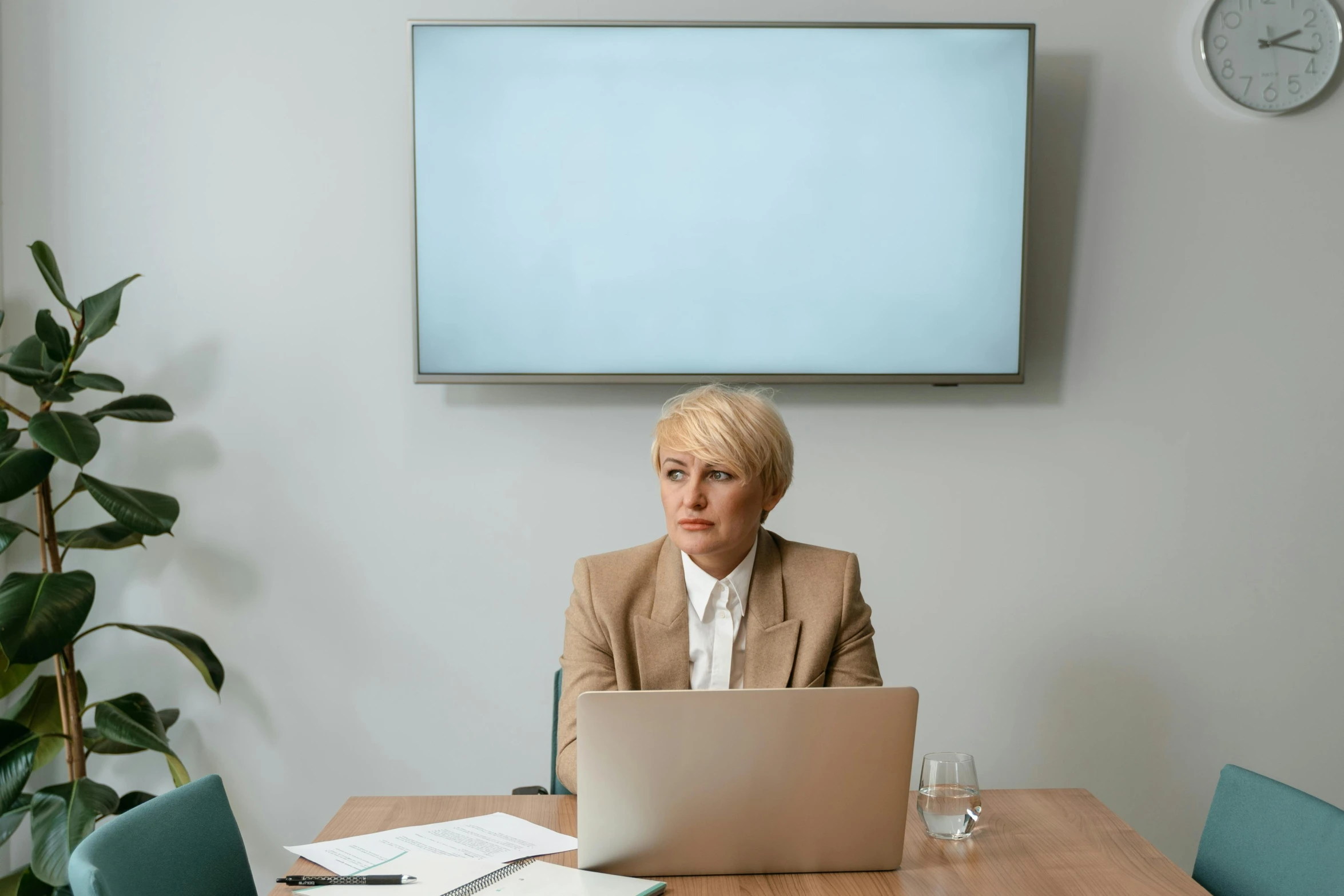 a woman sitting at a table in front of a laptop computer, human staring blankly ahead, in a meeting room, large screen, blonde women