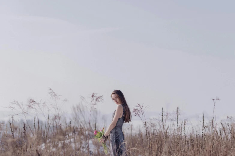 a woman standing in a field holding a bunch of flowers, inspired by Anka Zhuravleva, pexels contest winner, winter setting, plain background, medium format. soft light, grey