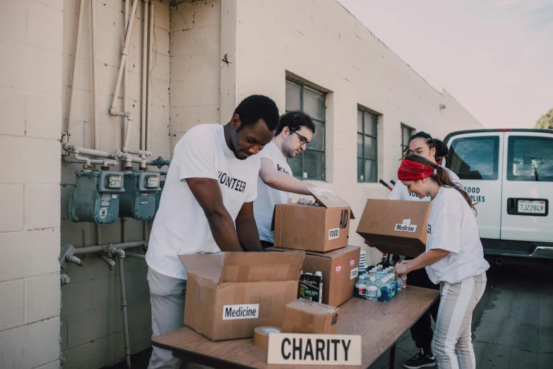 a group of people standing around a table filled with boxes, a friend in need, ye mighty, los angeles, profile image