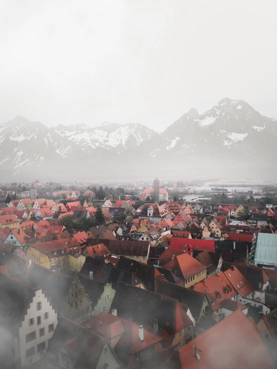 a view of a town with mountains in the background, pexels contest winner, rainy and foggy, germany. wide shot, captured on iphone, red roofs