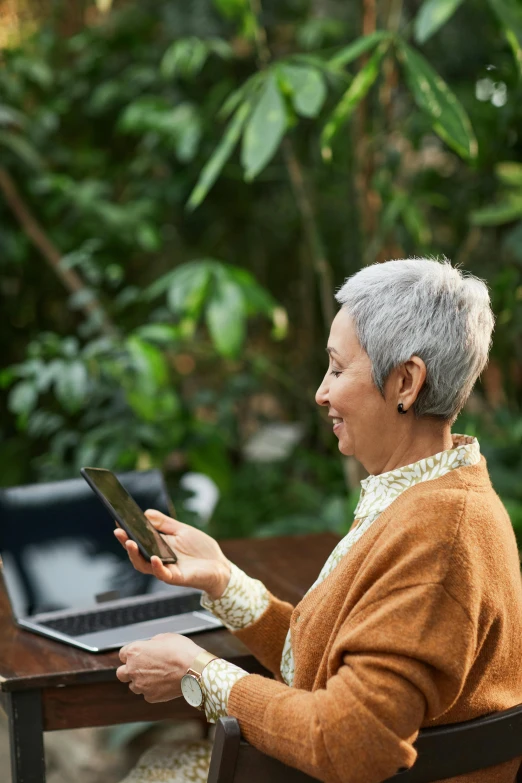 a woman sitting at a table using a laptop computer, happening, buzz cut gray hair, lush surroundings, mobile, profile image