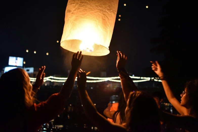 a group of people holding up a sky lantern, a photo, lights in distance, crisp details, fireball hand, profile image