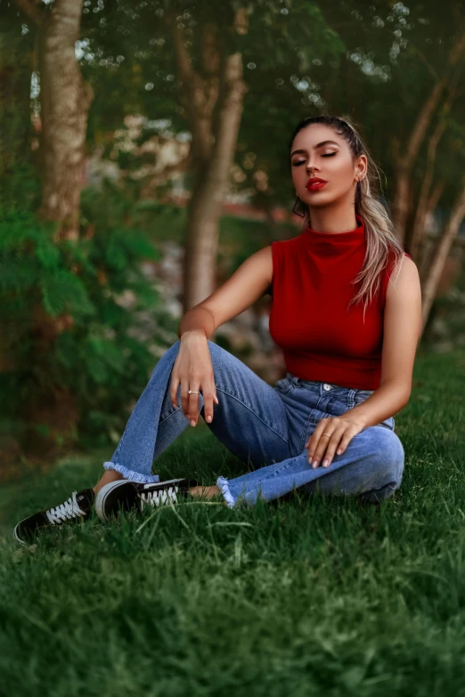 a woman sitting on top of a lush green field, an album cover, inspired by Elsa Bleda, trending on pexels, jeans, red tank-top, shady look, tanned ameera al taweel