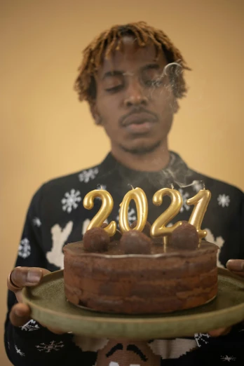 a man holding a cake with the number 2021 on it, an album cover, by Winona Nelson, trending on unsplash, hyperrealism, smoking weed, black teenage boy, video still, new years eve