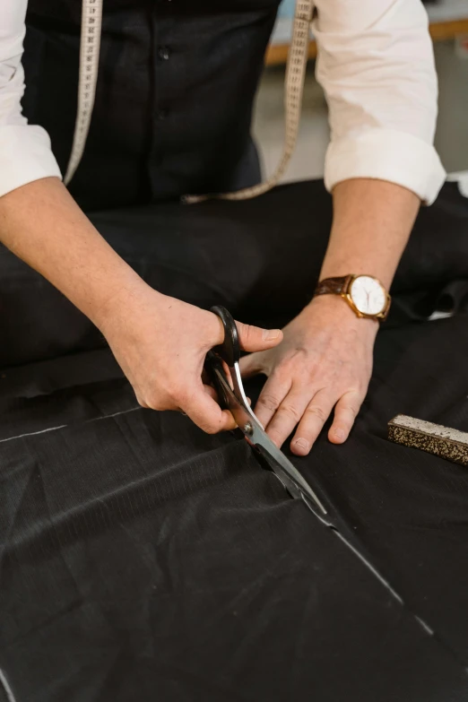 a person cutting fabric with a pair of scissors, a man wearing a black jacket, detailed product shot, caparisons, multi-part