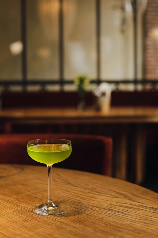 a green cocktail sitting on top of a wooden table, by Ndoc Martini, multiple stories, julia hetta, cocktail bar, sake