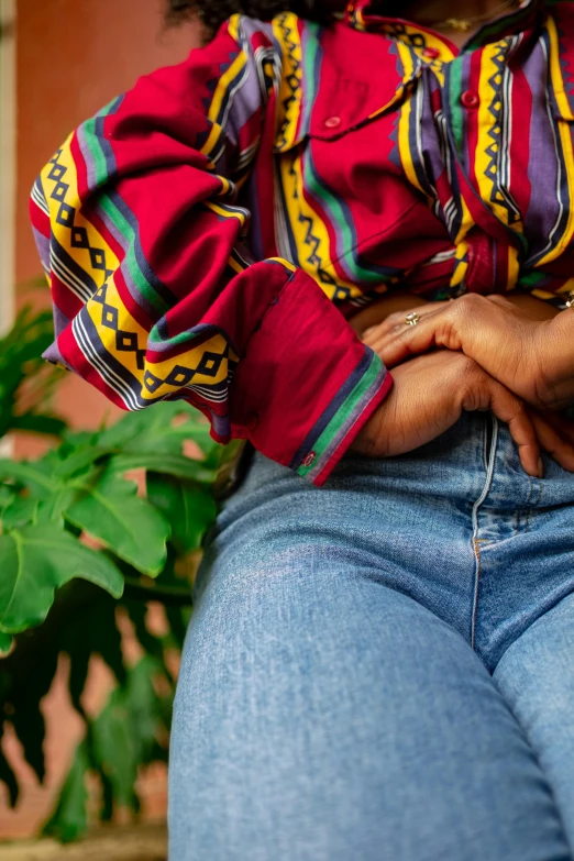 a close up of a person sitting on a bench, midriff, colourful clothing, next to a plant, wearing a shirt and a jean