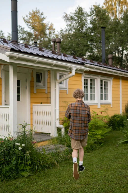 a woman walking in front of a yellow house, a picture, inspired by Eero Järnefelt, unsplash, young male with walking stick, cottage, production still, exterior view