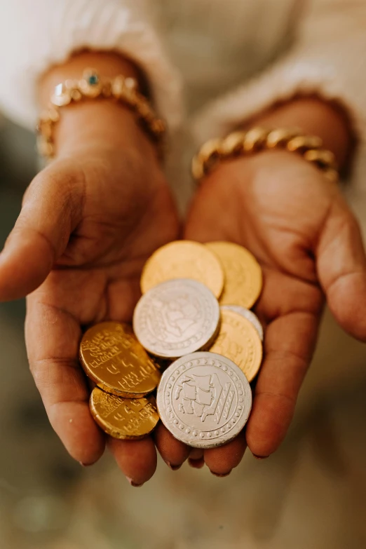 a person holding a bunch of coins in their hands, by Julia Pishtar, trending on unsplash, renaissance, arab inspired, instagram story, gold silver, ethiopian