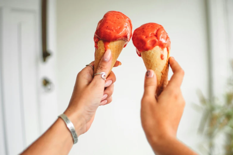 two people holding up two ice cream cones, by Julia Pishtar, pexels contest winner, coral red, glossy finish, made of glazed, ready to eat