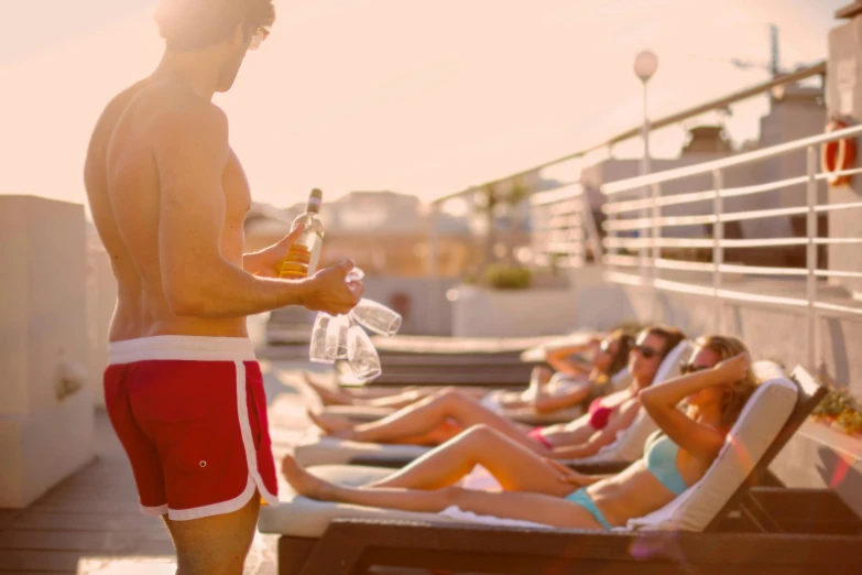 a man standing on top of a roof next to a group of people, by Carlo Martini, pexels contest winner, in a sun lounger, holding a drink, boutinela bikini, profile image