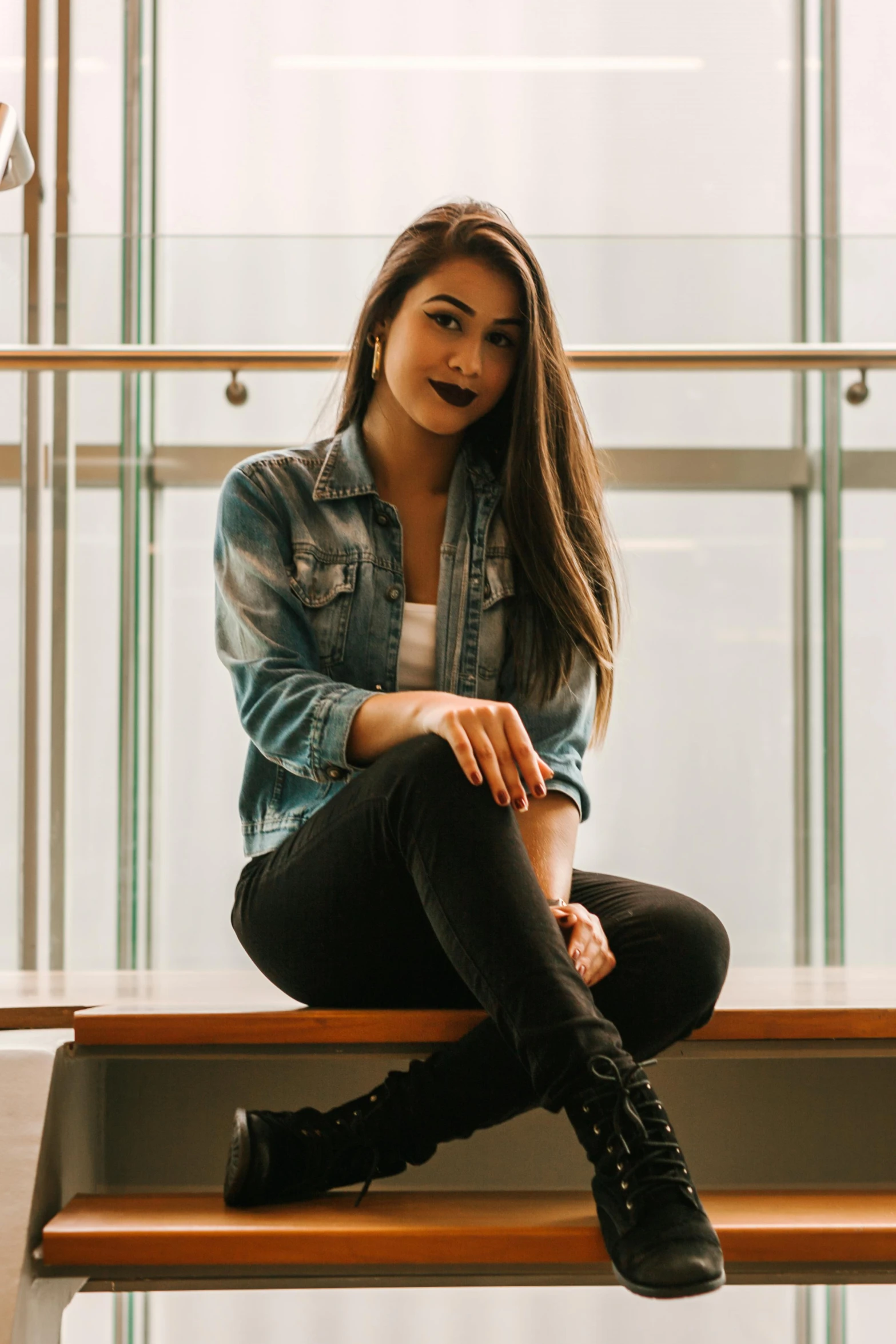 a woman sitting on top of a wooden bench, by Robbie Trevino, wearing a jeans jackets, avatar image, indoor picture, student
