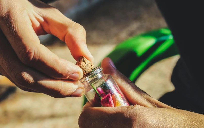 a close up of a person holding a small bottle, pexels contest winner, process art, picking up a flower, sand art bottle, candy treatments, upcycled