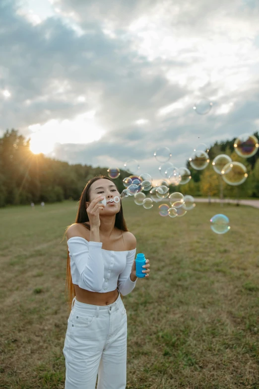 a woman blowing bubbles while standing in a field, by Adam Marczyński, pexels contest winner, beautiful young asian woman, bottle, foamy bubbles, 🤬 🤮 💕 🎀