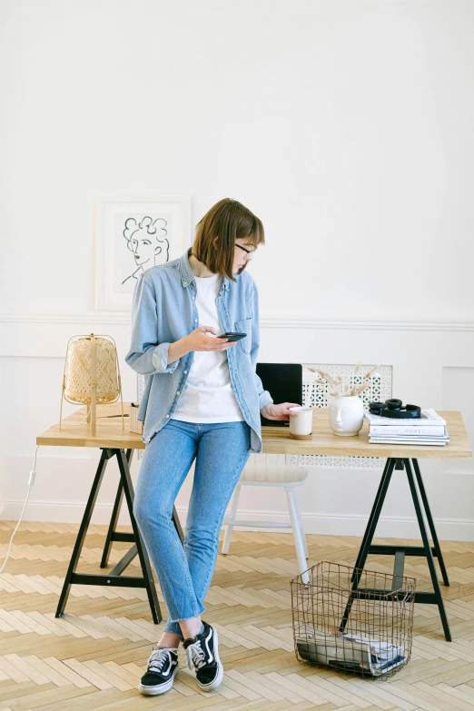 a woman sitting at a desk using a cell phone, trending on pexels, arbeitsrat für kunst, fullbody photo, standing, wearing denim, minimalist home office