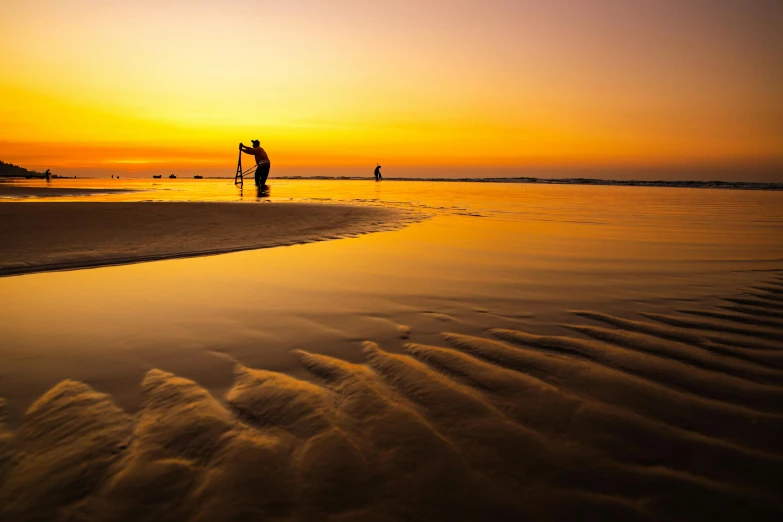 a couple of people standing on top of a sandy beach, by Ibrahim Kodra, unsplash contest winner, fishing, liquid gold, low sunset, ripples