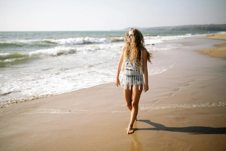 a woman walking on a beach next to the ocean, pexels contest winner, aztec bathing suit, teenage girl, full body length, people walking around