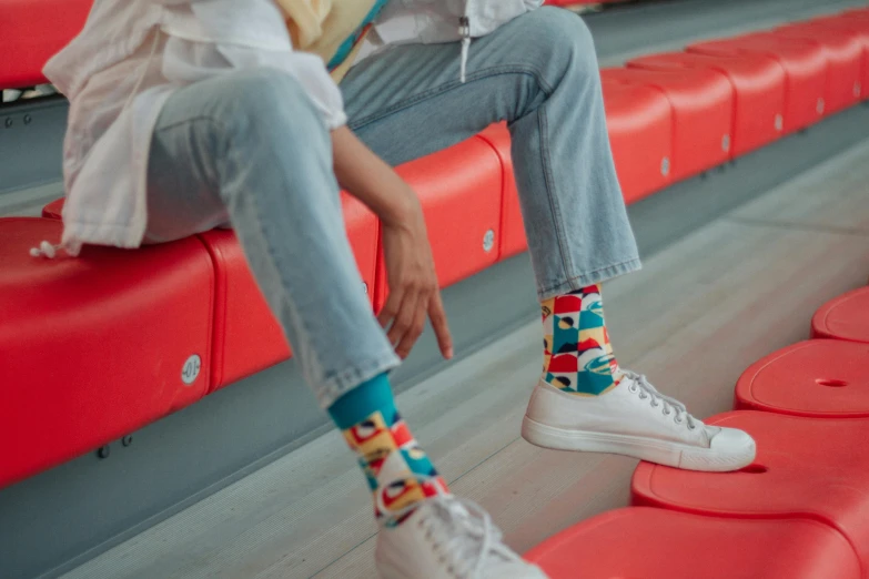 a woman sitting on top of a red bench, by Emma Andijewska, pexels contest winner, maximalism, socks, standing in a stadium, graphic print, sitting in a lounge