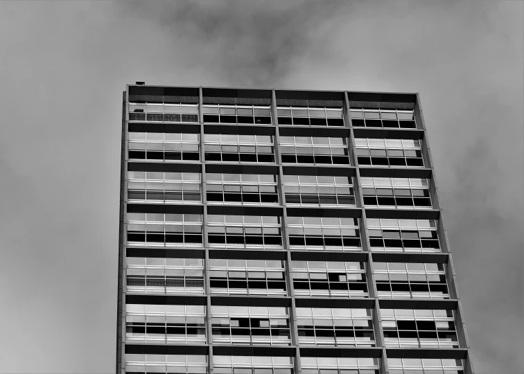 a black and white photo of a tall building, inspired by Richard Wilson, unsplash, brutalism, wellington, fire from some windows, taken on a 1960s kodak camera, low angle!!!!