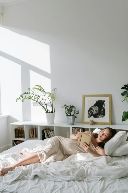 a woman laying on a bed reading a book, pexels contest winner, light and space, clean and pristine design, plants, small bedroom, promo image