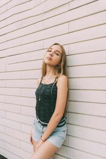 a young woman leaning against a white wall, an album cover, trending on pexels, photorealism, she is wearing a black tank top, sydney sweeney, wearing casual clothing, profile pic