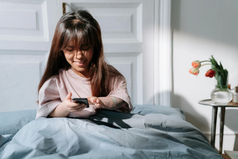 a woman sitting on top of a bed holding a cell phone, a cartoon, trending on pexels, young child, asian girl with long hair, playing games, bed