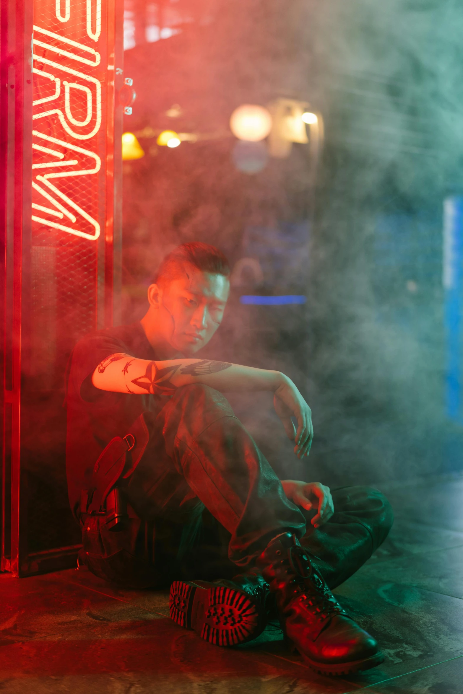 a man sitting on the ground in front of a neon sign, inspired by Liam Wong, mangeta smoke red light, male model, justin sun, scene from bladerunner movie