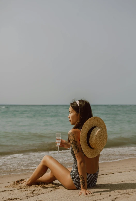 a woman sitting on top of a sandy beach next to the ocean, wine, profile image, vietnamese woman, uncropped