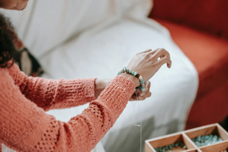 a woman sitting on a couch next to a red couch, by Emma Andijewska, trending on pexels, made of beads and yarn, turquoise jewelry, blessing hands, sitting on edge of bed
