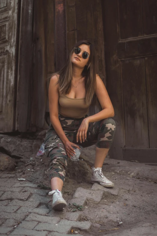 a woman sitting on the ground in front of a building, trending on pexels, jungle camo, with sunglass, fully body pose, portait photo profile picture