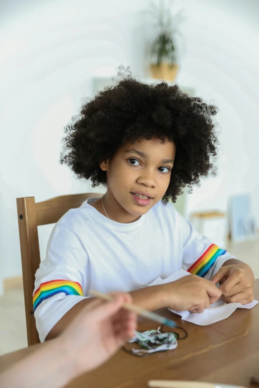 a little girl sitting at a table in front of a man, afro hair, rainbow accents, holding pencil, gen z