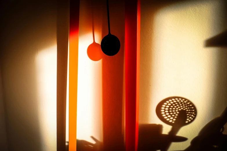 a shadow of a person holding a tennis racquet, an abstract sculpture, inspired by Alexander Calder, unsplash, light and space, orange lamp, hanging out with orbs, against a red curtain, light glare