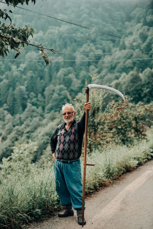 a man standing on the side of a road holding a scythe, by Muggur, pexels contest winner, grandfatherly, in the hillside, russian style, 🚿🗝📝